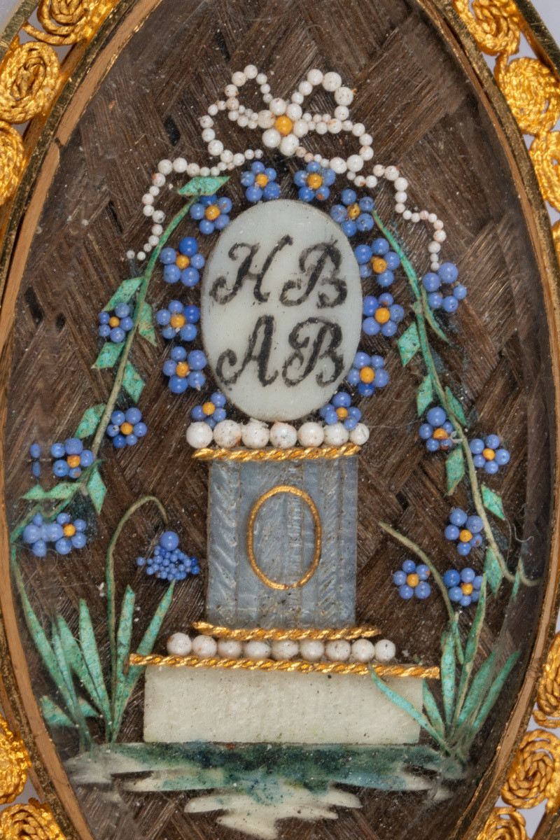 Minnestøtte/søyle med initialene til Henrik Dinclow Bruun og Anne Marlene Bruun . Perler formet som blå blomster, forglemmegei, og grønt gress rundt fundamentet på søylen