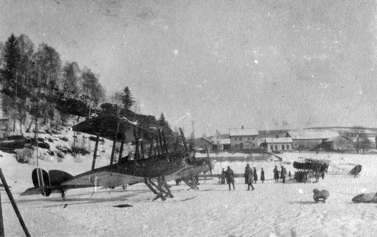 Fly og flygere oppstil på den islagte Mjøsa under Hærens flyvesens vinterøvelse på Lillehammer i 1920. Nærmest et britisk rekognoseringsfly av typen BE 2E og lengst til høyre en Farman Shorthorn. Det kan være Vingnes gård som ses i bakgrunnen.