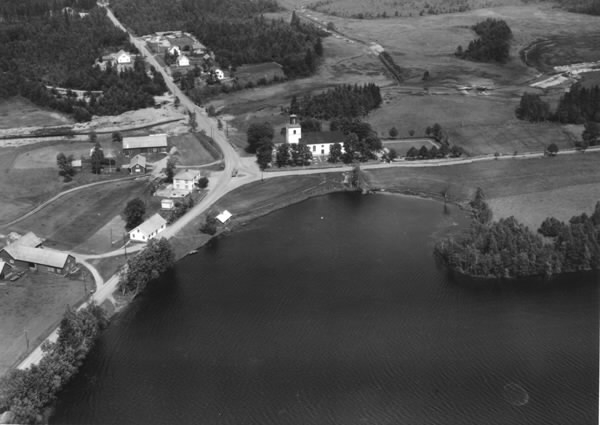Flygbild över Krogsered. Vägkorsningen vid Krogsereds kyrka och kyrkogård invid Lyngsjön. Gårdar och villor längs vägarna.