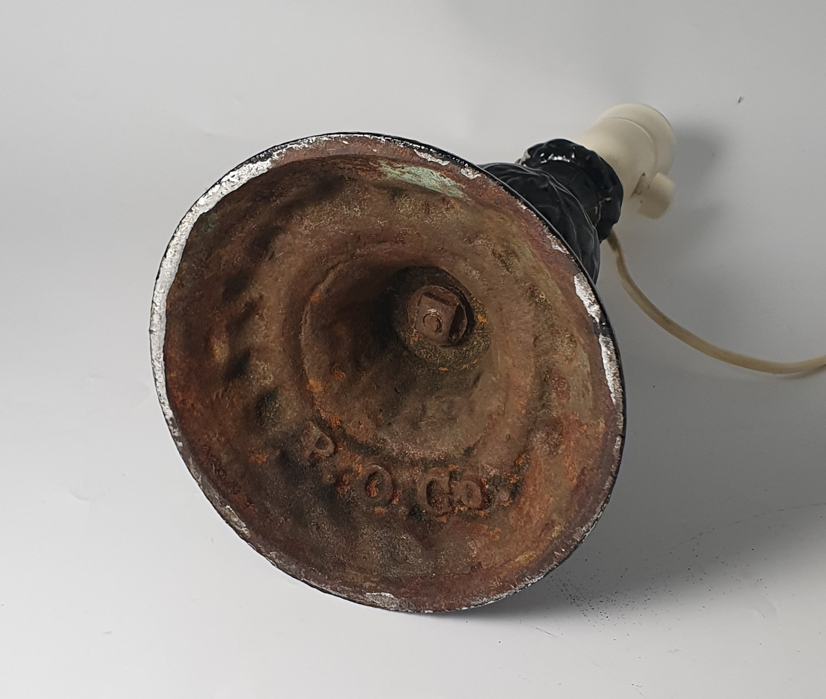 Elektrisk lampe med støpt fot fra Mandals Værksted, et støperi på Sanden i Mandal. Lampeføttene ble produsert for Mandal Paraffin Olie Co. på Risøbank ved Mandal. Parafinoljefabrikken var virksom fra 1862 til 1872.