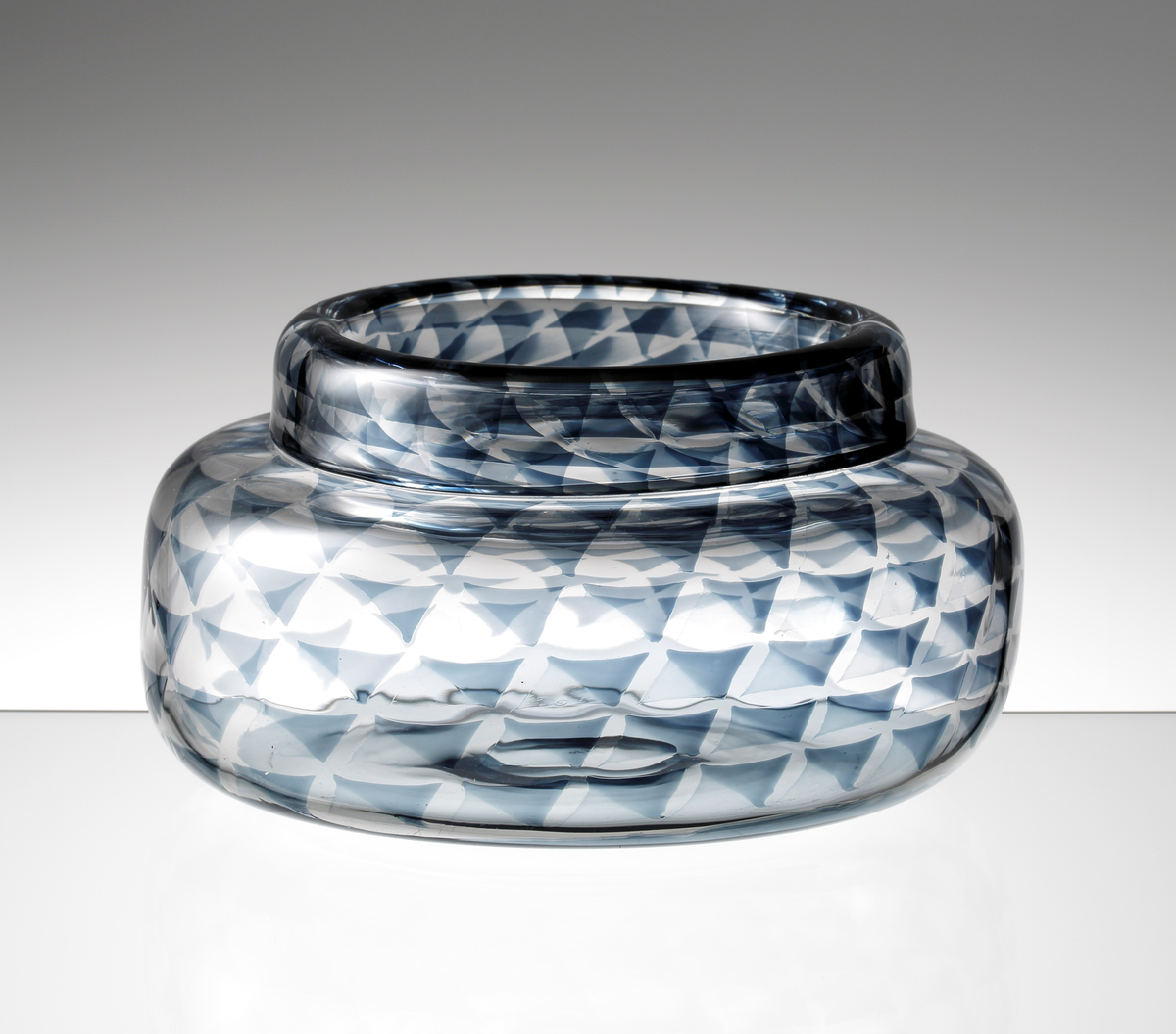 Formgiven av Ingeborg Lundin. Graalvas med låg cylindrisk form och omvikt mynningskant. Utförd med gråblått
geometriskt mönster.