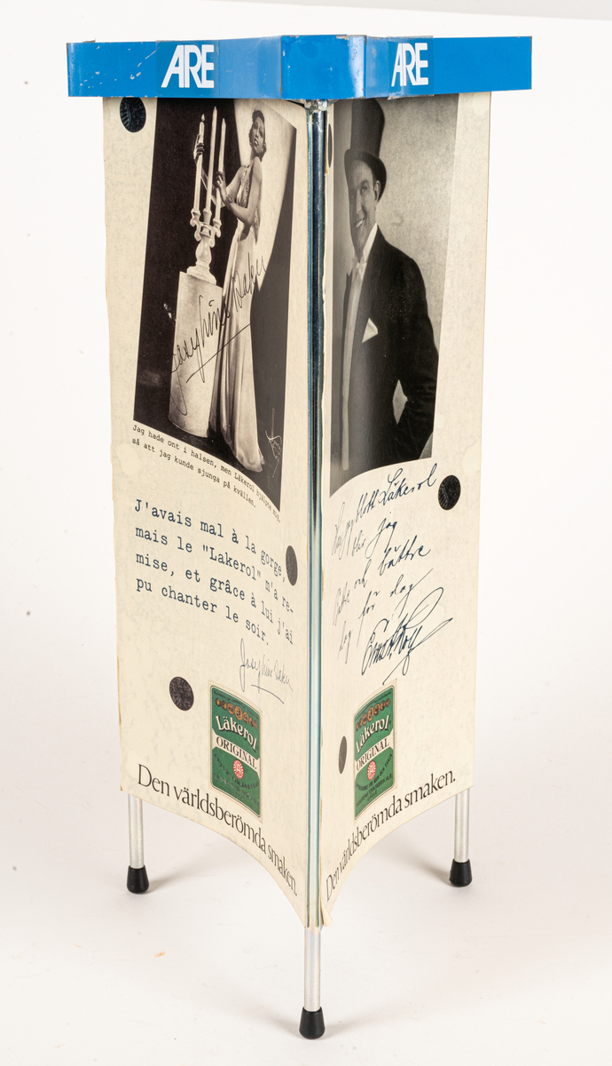 Reklamskylt, reklampelare på tre ben med plastfötter, i metall och papp, för Läkerol. Intygsreklam med citat från tre kändisar: Joséphine Baker, Ernst Rolf och Maurice Chevalier på de tre sidorna.