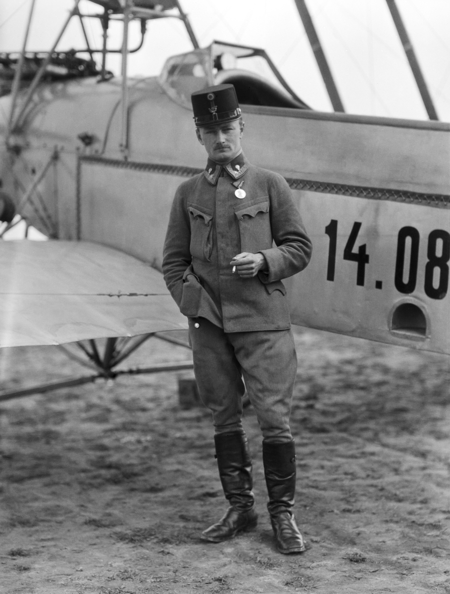Porträttfoto av militär flygare från Österrike-Ungern framför flygplan Lohner B.III märkt nummer 14.08. Flygaren bär en cigarett.