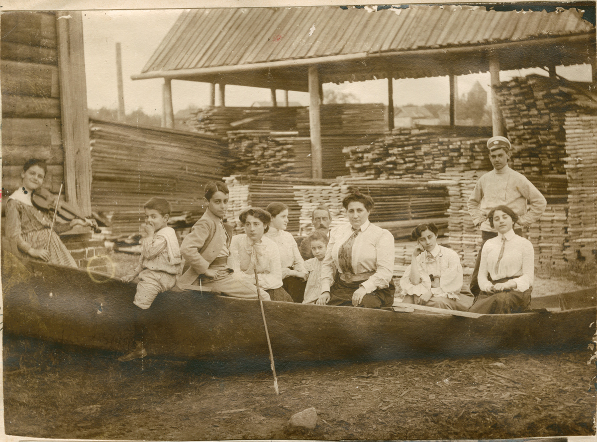 Motivet viser familien Rostin i en båt på land ved teglsteinfabrikken i Borovichi. Til venstre i bildet er Victoria med fiolin, Nikolaj, Ignazy, Valentine, Julia, Serafima, mor Sonja, Florentine og Elisabeth. Mennene er ukjente.
