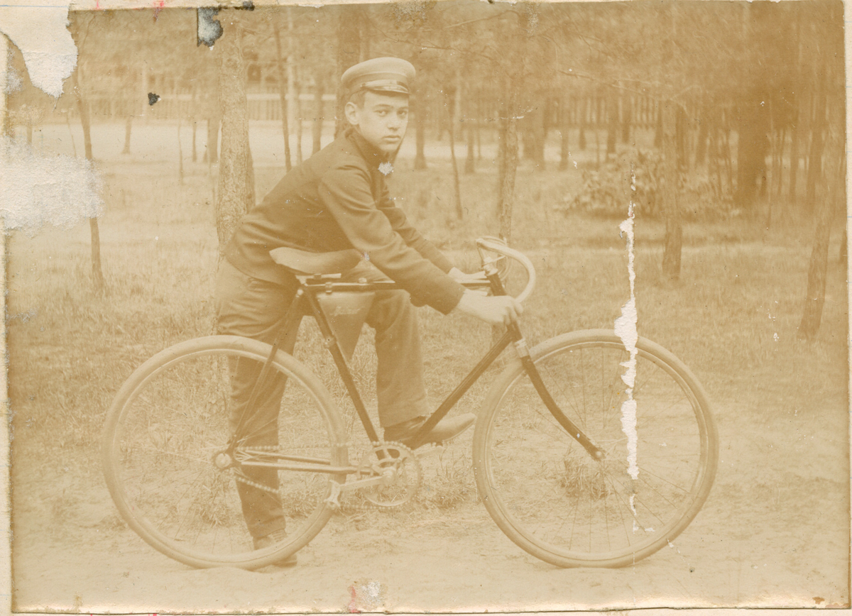 Motivet viser en ung mann som poserer med en sykkel. Han har det ene beinet plassert på pedalen og den andre på bakken. I bakgrunnen ses flere trær og et gjerde som rammer inn området.