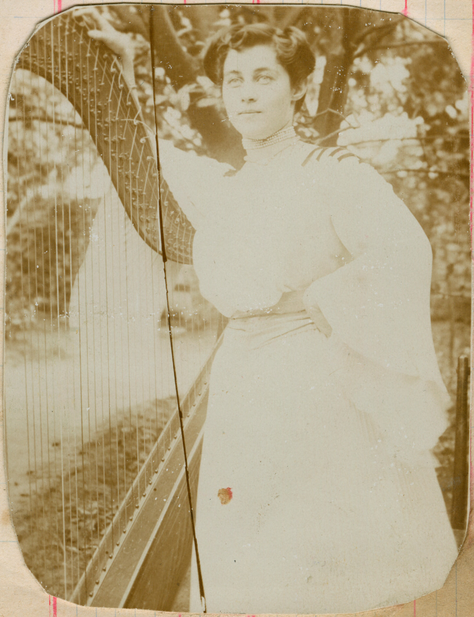 Utendørsportrett av Florentine Rostin med en harpe. Hun er ikledd en hvit kjole med vide ermer og et stramt halskjede med perler.