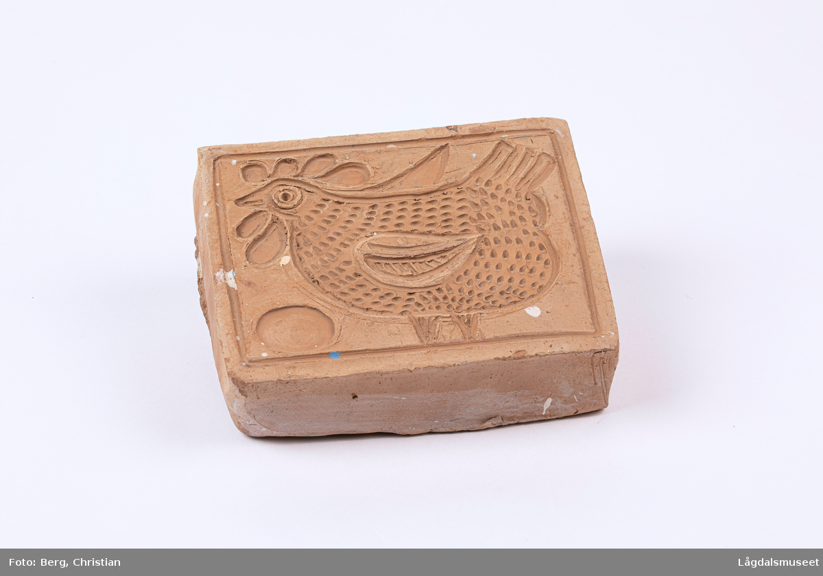 Trykkblokk i keramikk for enkelt å påføre dekorelement på fat og lignende. Motivet er ei høne og et egg.