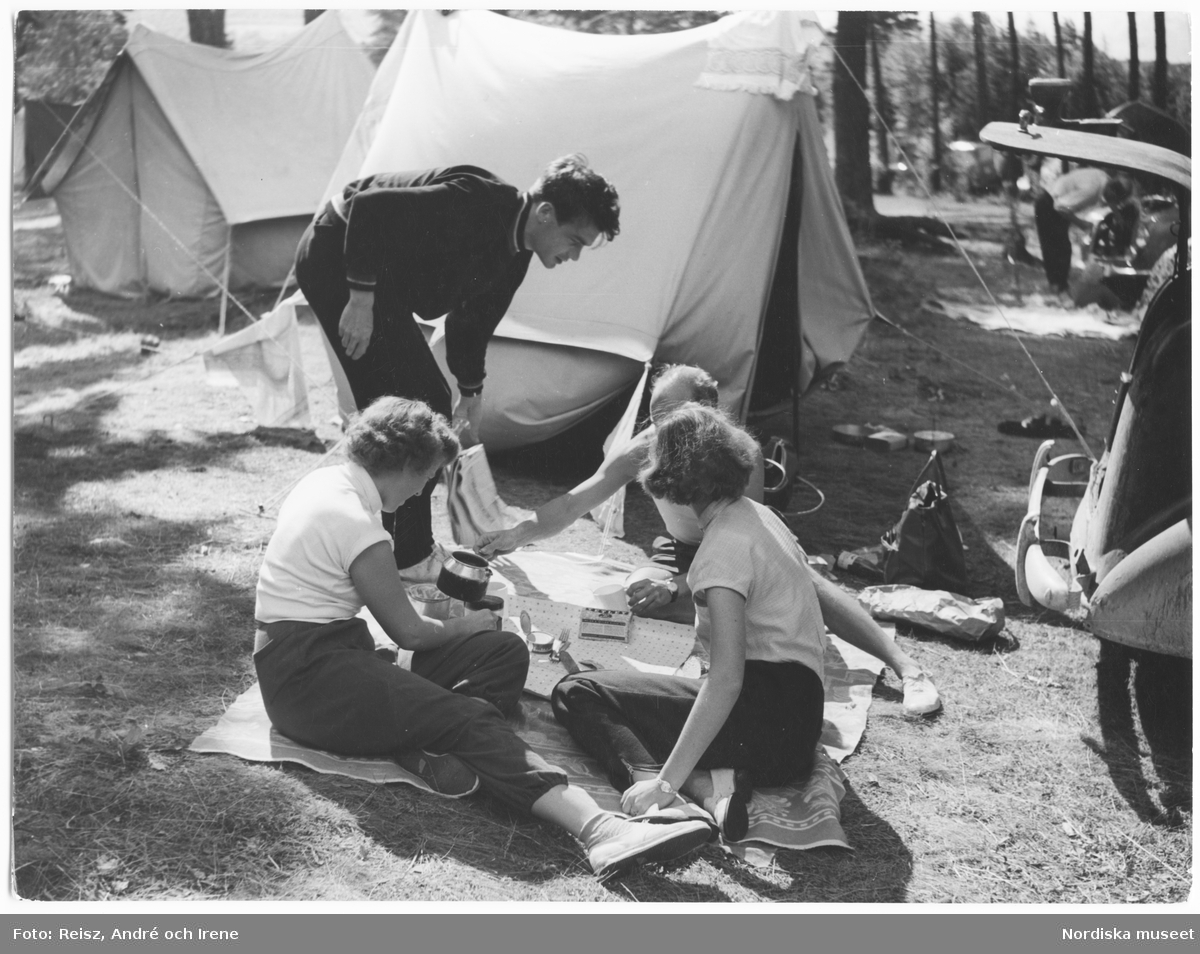 Ett sällskap äter lunch på en camping i Dalarna. Möjligen Sofiaflickan Marika Forsberg med sällskap? jfr NMA.0106506 samt NMA.0106516.