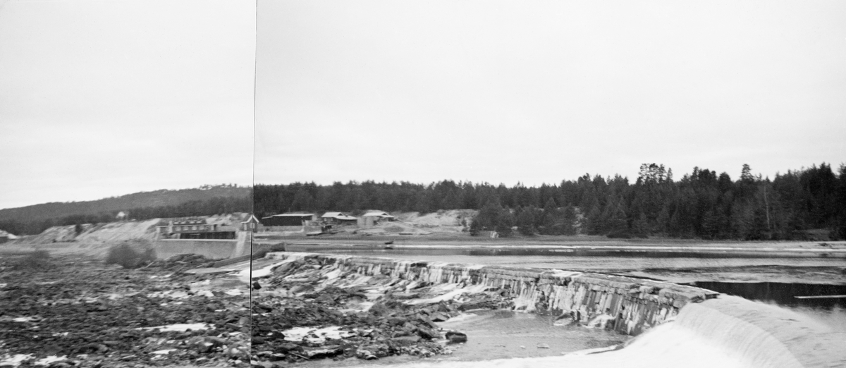 Fra dammen som stuvet opp vann til kraftverket ved Skjefstadfossen i Glomma, i Heradsbygda i Elverum. Fotografiet ble tatt høsten 1939, og det er montert som den høyre delen av et panoramabilde i et av Glomma fellesfløtingsforenings album (jfr. SJF.1989-03535). Her ser vi overløpsdammen, som var 312 meter lang, og litt lavere i den østre enden (til høyre på dette bildet) enn i den vestre. Denne løsningen ble valgt for å skape et drag i vannet som trakk fløtingsvirket mot den østre delen av elveløpet, der det var noe djupere enn i den midtre og vestre delen, og følgelig noe mindre fare for at stokkene skulle sette seg fast og pakkes sammen i hauger som det ble krevende og farlig for fløterne å løsne.