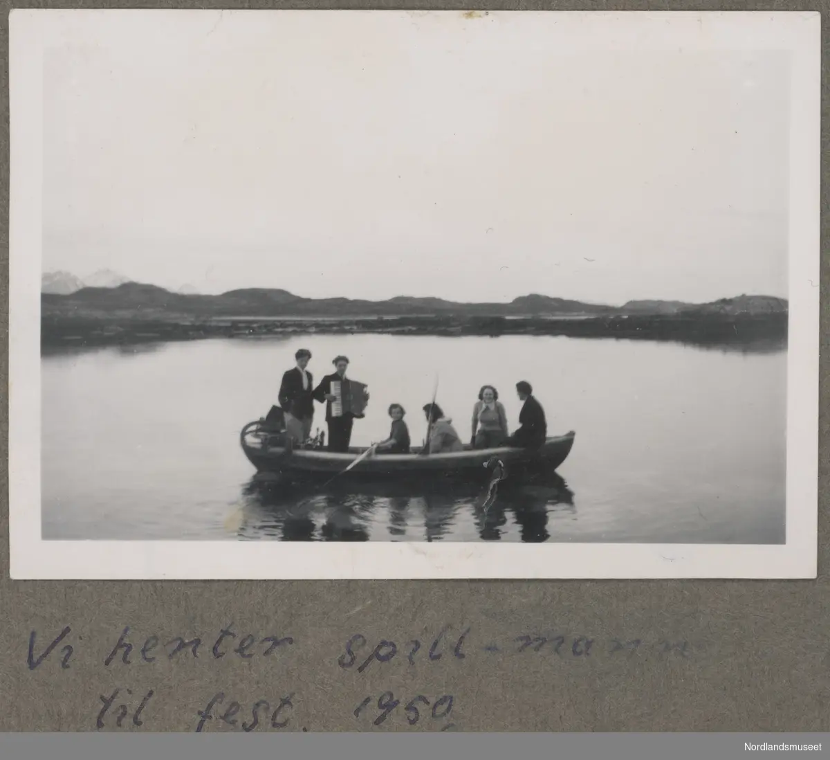 Seks ungdommer i en robåt, en med trekkspill, sykkel lastet i båten