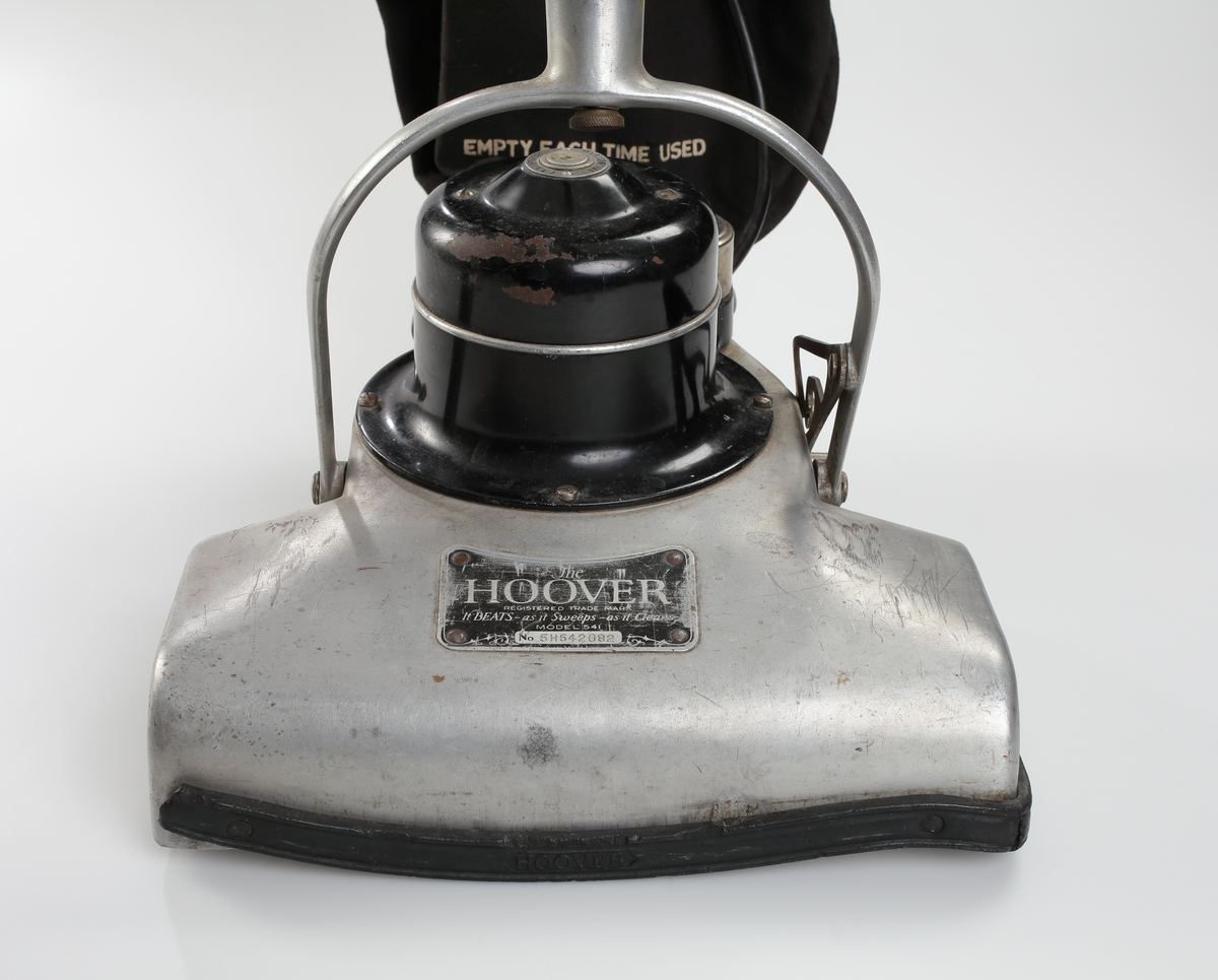 Elektrisk dammsugare av märket The Hoover, tillverkad i USA mellan åren 1923-25. Dammsugaren består av ett sugmunstycke på fyra mindre hjul och med roterande borste. Motorn är placerad ovanpå munstycket. Från sugmunstycket leder ett fällbart/ledat skaft samt en monterad textil dammsugarpåse som går att lossa och haka av vid tömning.
