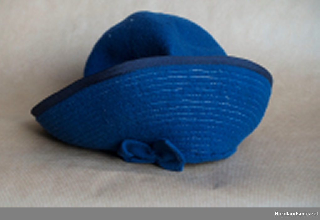 Liten blå filthatt, damehatt eller jentehatt, opprettet kant med blå filtsløyfe foran og bak. Tynt gummibånd til å feste under haken.