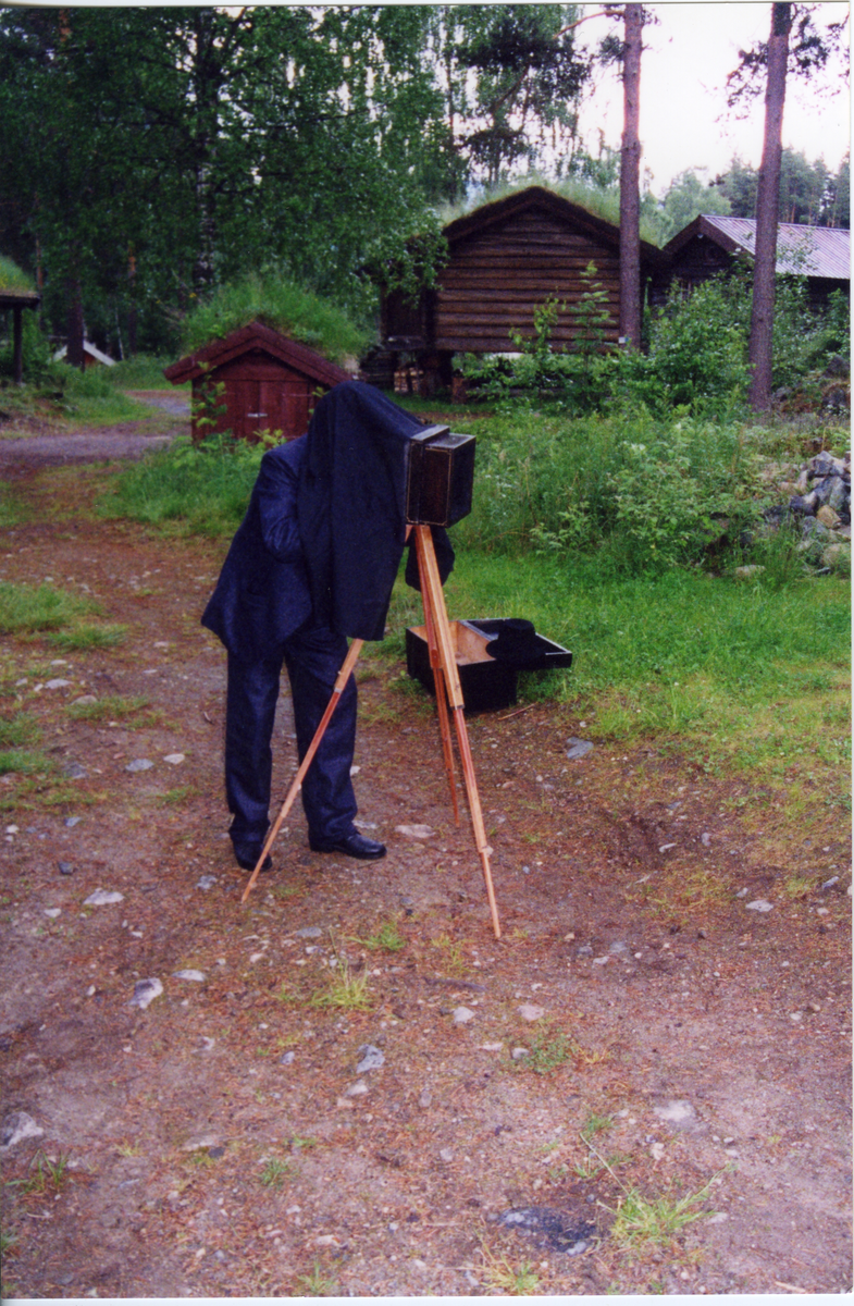 Emigrantspelet. Mann/Bjørn Gulbrandsen tar bilder med gammelt kamra. Han står inne i stativet.
