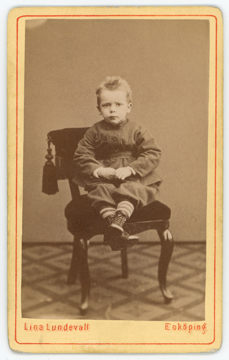 Svartvit porträtt av en okänd pojke sittande på en stol.