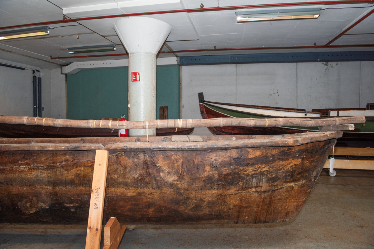 Stor, uthult trestamme. Stokkbåt med skrog bygget oppav flere deler. Rundholt m.m. av bambus. To stk støttebrett (utriggere).
