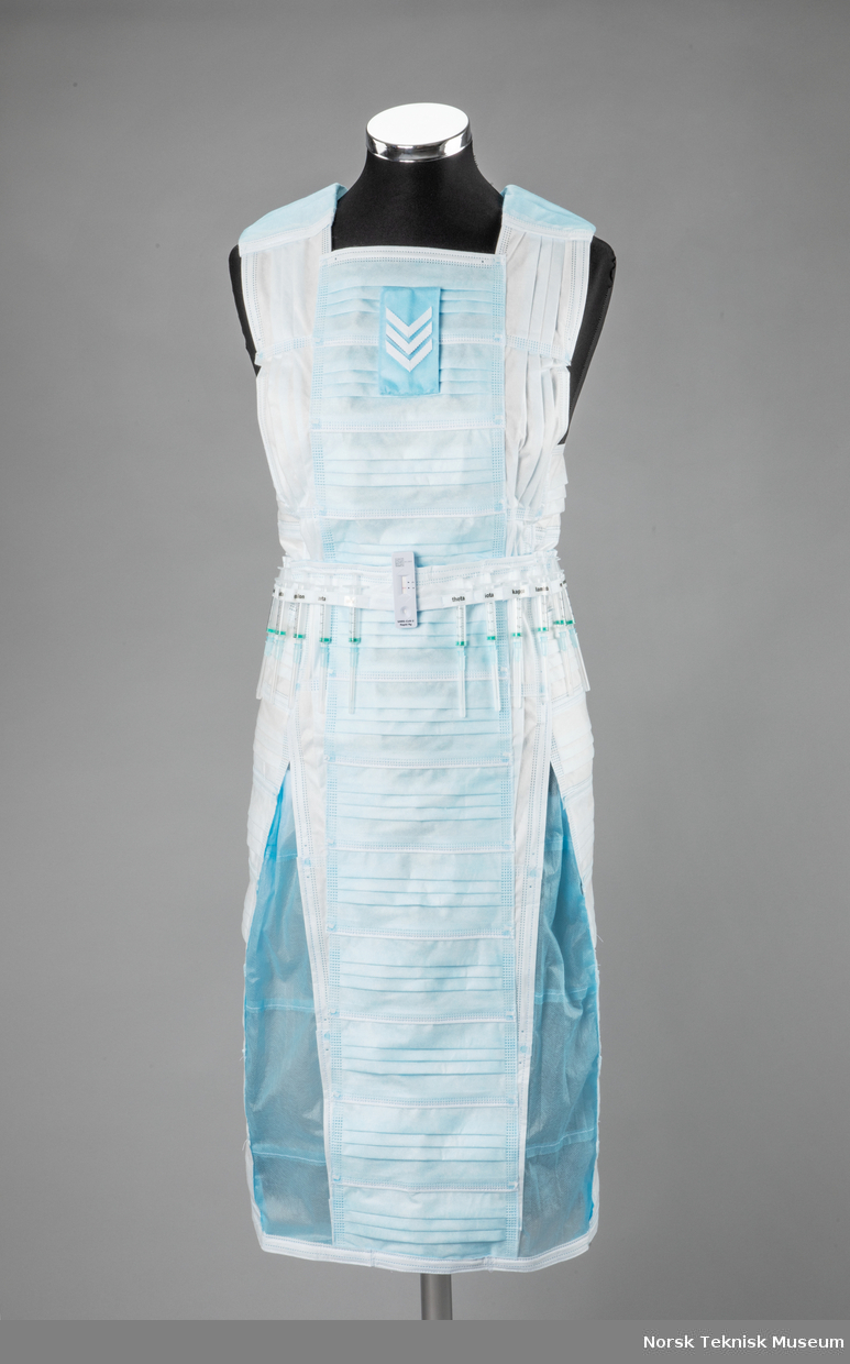Kjole laget av munnbind på kjolestativ. Kjolen har et belte laget av vaksinesprøyter og en koronatest, med greske bokstaver for å representere stammer av koronavirus.