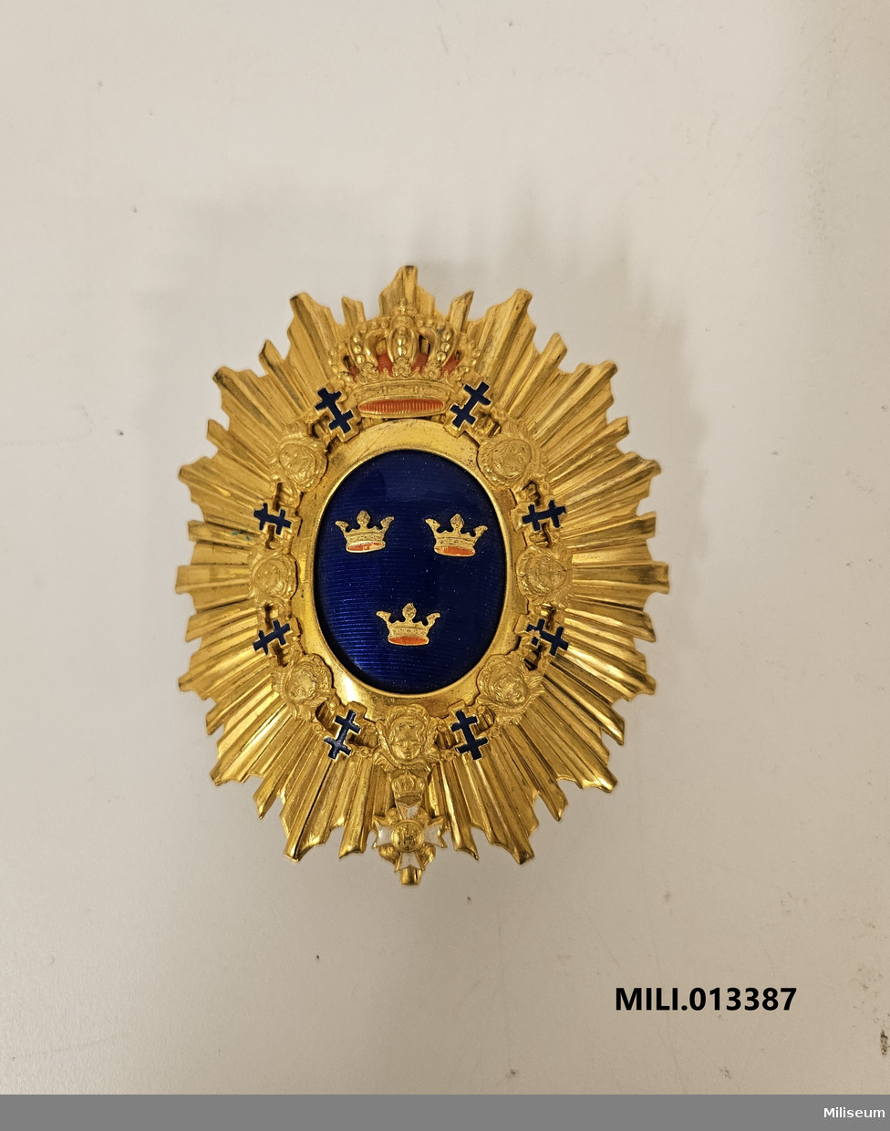 Emblem m/1880 till käppi m/1880, av förgylld mässing. Med fastlödd pompong.