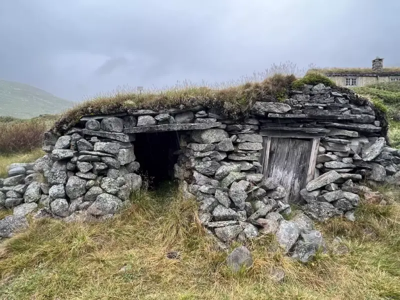 Steinbygning i naturstein, med to dørar og torv på toppen