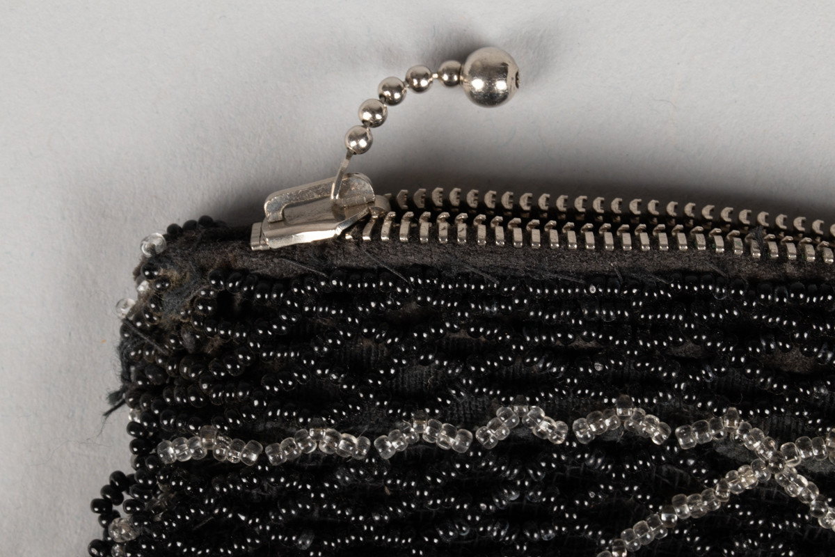 Pung med glidelås. Utenpå er det sydd fast perler som er perlet sammen til et eget mønster som ligger utenpå selve stoffet.
