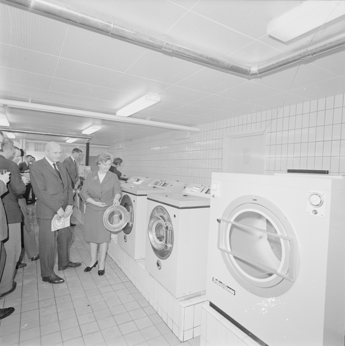 Kvinna och män i tvättstuga med flera tvättmaskiner.