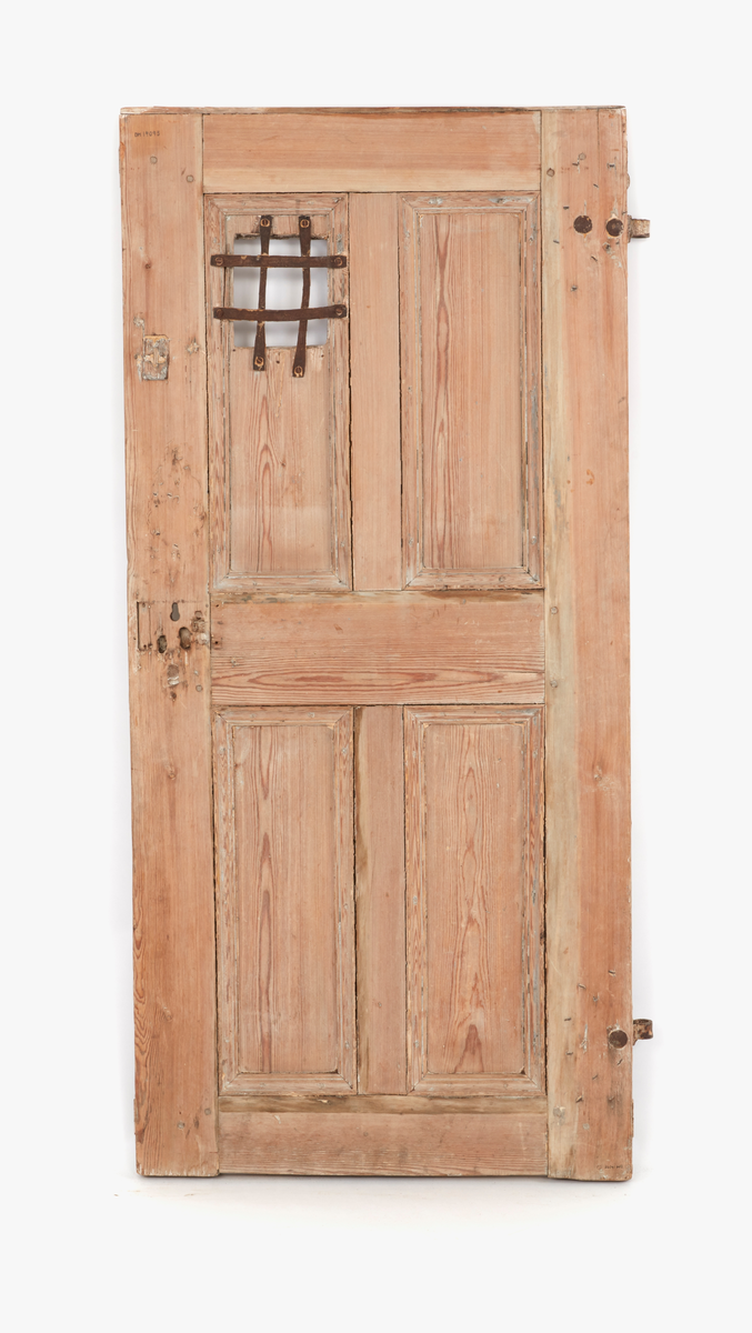 Dörr av furu, skuret och pluggat.
Tjocklek: 40 mm.
I övre vänstra dörrspegeln en fyrkantig öppning, stängd med ett galler av fyra järnkrampor, två fastsatta lodrätt och två vågrätt.