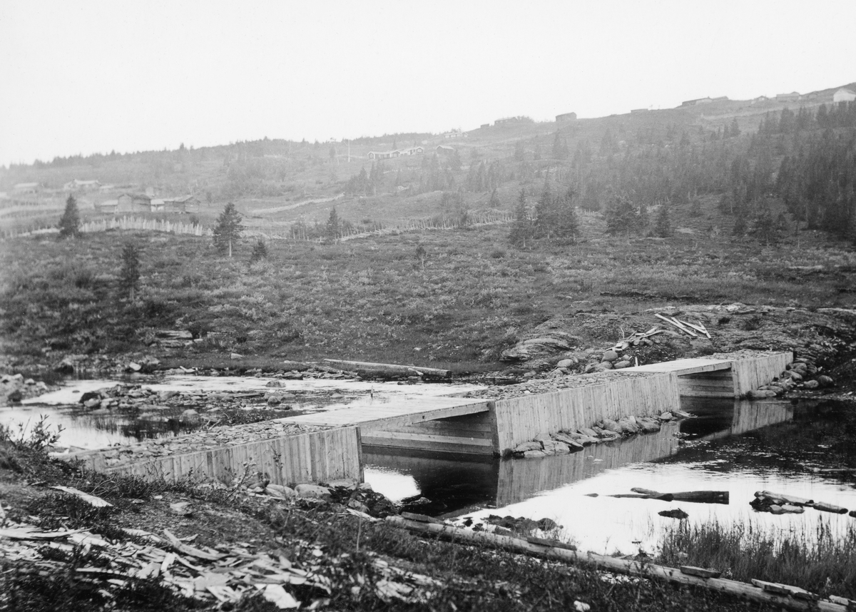 Håkåsæterdammen i Sør-Fron kommune i Oppland, fotografert våren 1936, med de nevnte sætrene i bakgrunnen. Dette var en tømmerkistedam med to løp der sideveggene i løpet var plankekledde. Dette var en «nåledam», som da bildet ble tatt sto åpen, slik at vannet strømmet gjennom damløpene. Nålene var planker som, når dammen skulle stenges, ble stukket i motstrøms retning, slik at de ble stående som en tett vegg som vannet presset mot en terskelstokk på elvebotnen og dambruas overkant. Håkåsæteråa kommer fra Fagerlivatnet i grensetraktene mellom Nord- og Sør-Fron kommuner.  Dette er det øverste tilløpet til den vestre delen av Gausavasseraget, som renner gjennom Vestre Gausdal og Follebu, og renner ut i Gudbrandsdalslågen i Fåberg, en strekning på bortimot sju mil.