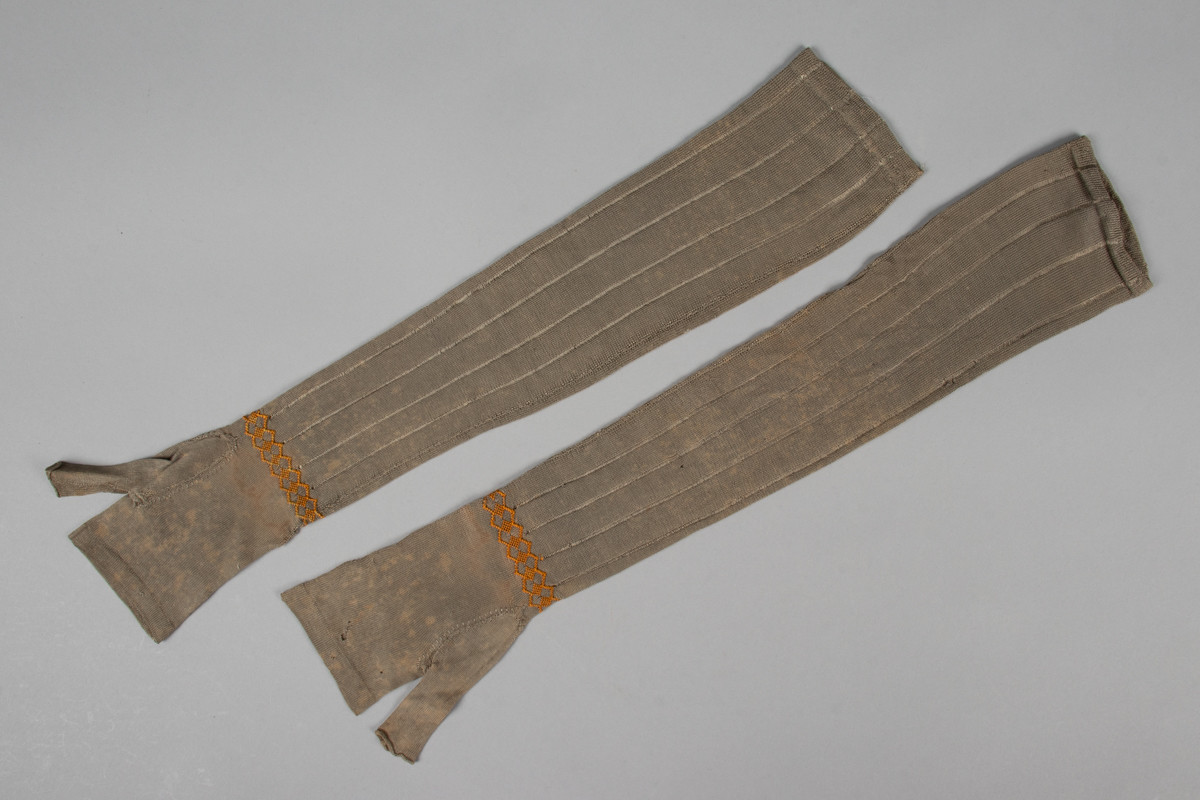 Et par lange, fingerløse hansker i glattstrikket silke med geometrisk silkebroderi rundt håndleddet