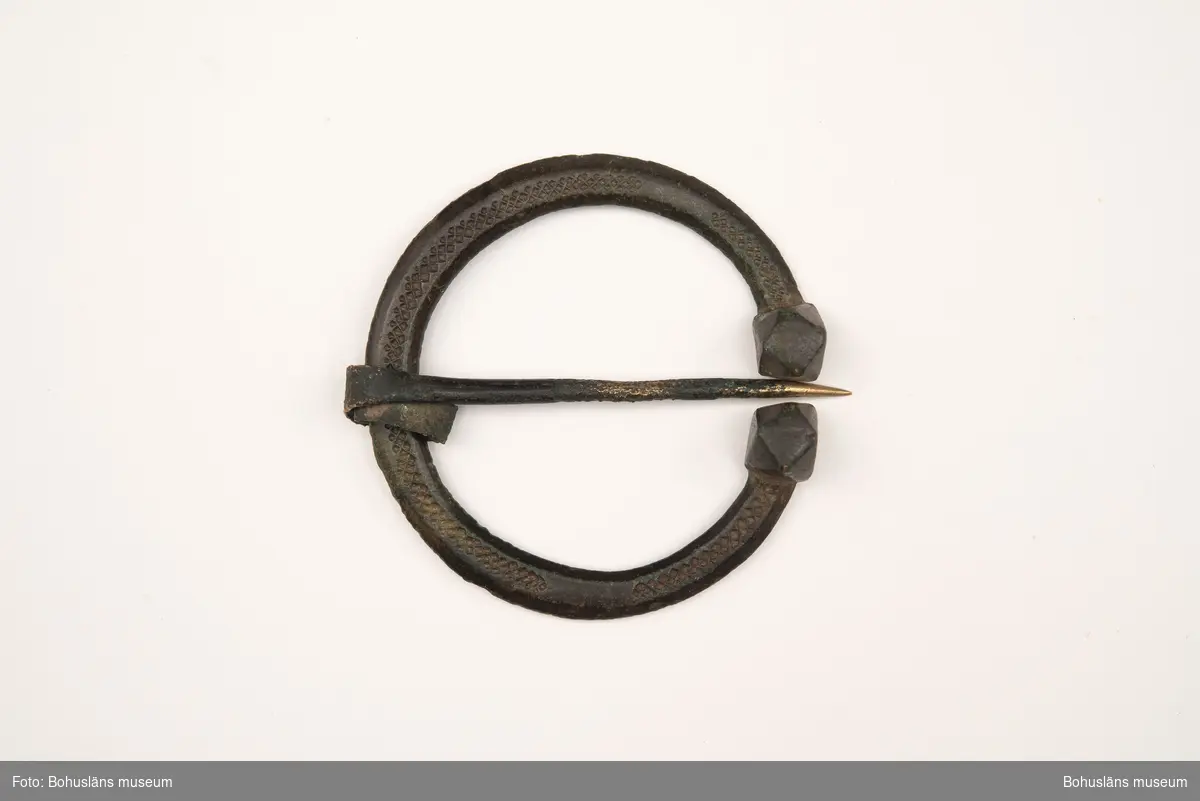 Hästskoformat ringspänne av brons, med dekor. En tillplattad rund bygel med fasetterade ändknoppar. Dekoren består av instämplade romber ovanpå bygeln. Nålens fäste är utplattad och upprullad runt bygeln.

Ringspännet är troligen från vikingatid, år 800-1050 e Kr. och användes för att hålla samman klädedräkten, exempelvis ett ytterplagg, en mantel, vid halsen. 

Citat ur brev som medföljde gåvan: "Brosch från bronsåldern - hittad av David Leonard Thorburn i jorden. Var?" (ur Agnes Thorburns anteckningar). 
Enligt Agnes bror, Thomas Thorburn, påträffades den troligen någonstans i Uddevallas omgivningar. David Thorburn var, enligt honom, känd bland bönderna som en person som köpte kuriosa. Thomas Thorburn skulle därför tro att någon bonde hittat den och sålt den till David Thorburn."
