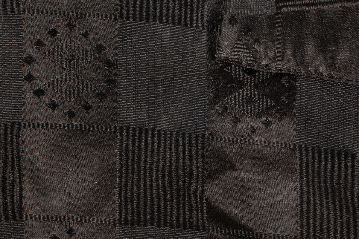 Håndsydd barnevest i svart silke i rutemønster. Vesten har høy krage. Forstykket er laget av svart silke. Bakstykket og for er laget av kvit strie. Vesten er omsydd, gjort smalere og kortere. Under armene er det sydd i en bit svart silke uten mønster. Vesten er slitt. slitasjeskade på innsiden av kragen. Reparasjon på venstre forstykke. To hull på bakstykket er lappet.