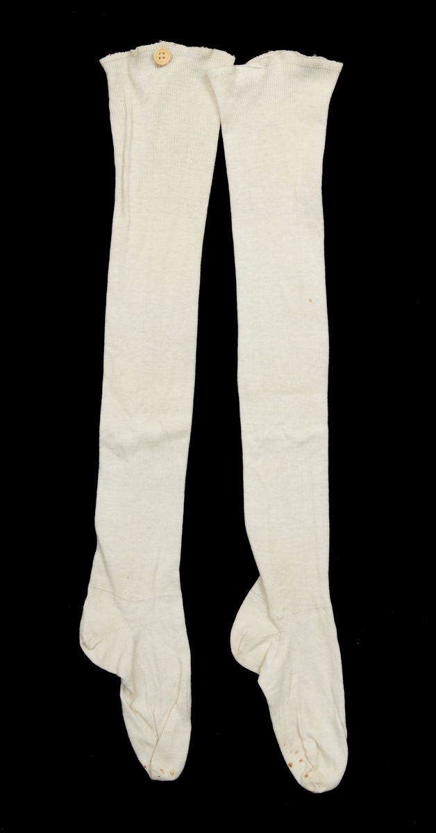 Ett par flickstrumpor, maskinstickade av vitt bomullsgarn. Lång modell med skaftet stickat i en rät och en avig maska, foten slätstickad. En knapp av ben på var strumpa för fastsättning. Användningstid 1910-tal.