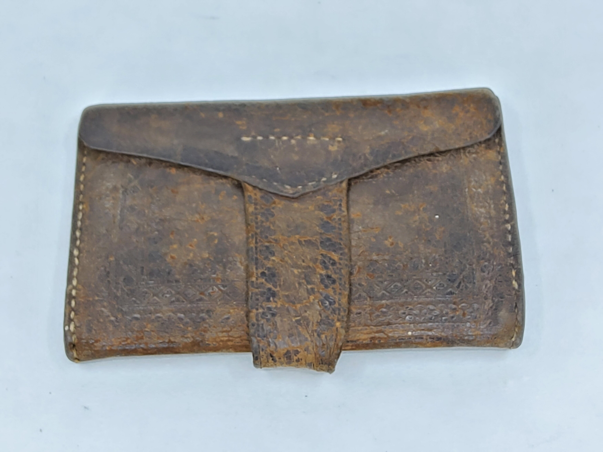 Plånbok, av brunt läder, med pressade mönster på ut- och insidorna fyra fack i olika format.