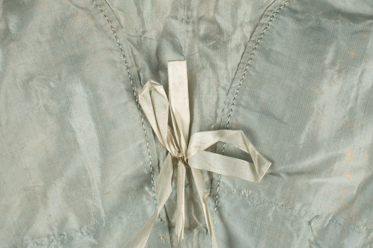 Håndsydd kjoleliv i empirestil, laget av lyseblå silke og foring i glanset linlerret. Korte puffermer og knyting foran.