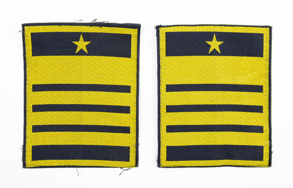 Ärmmatta, överste 1:a graden, med invävd gradbeteckning i gult på svart botten. Två stycken varav den ena har fastsydda kardborreband på baksidan.
