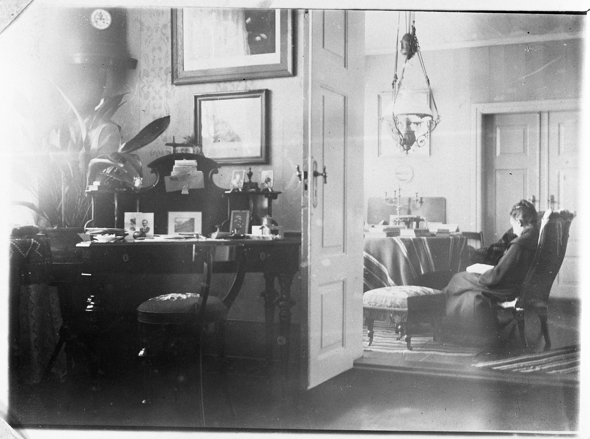 Interiørbilde fra Evenrud, Kapp i Østre Toten, ca. 1900. Bildet er tatt fra dagligstua, og med gløtt inn i hagestua der Thekla Raabe sitter i "damelenestol" og leser.