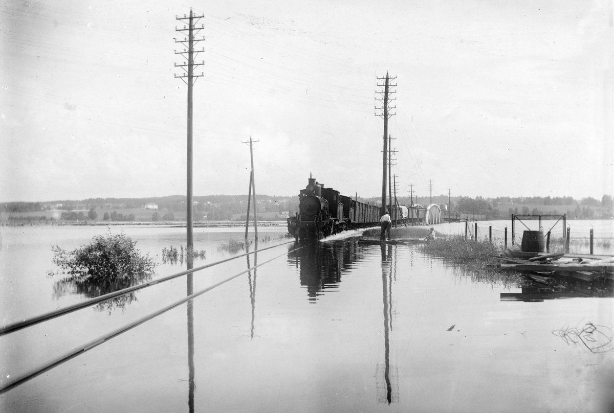 Hamar, Åkersvika, storflommen i Mjøsa 1927, jernbanebrua over Åkersvika. 14. Juli 1927. Damplokomotiv kjørende igjennom vannet. Vannstanden er 8, 24 over normalen, lysstolper,