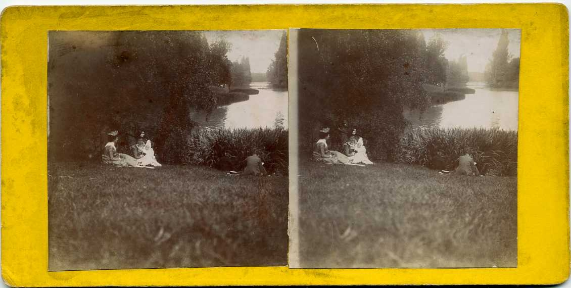 Två kvinnor sitter med ett litet barn i en grässlänt vid en damm. Det är Jeanne Machuron med dottern Marcelle samt hennes svärmor Céline Machuron. De befinner sig i en zoologisk park.
Stereobild.