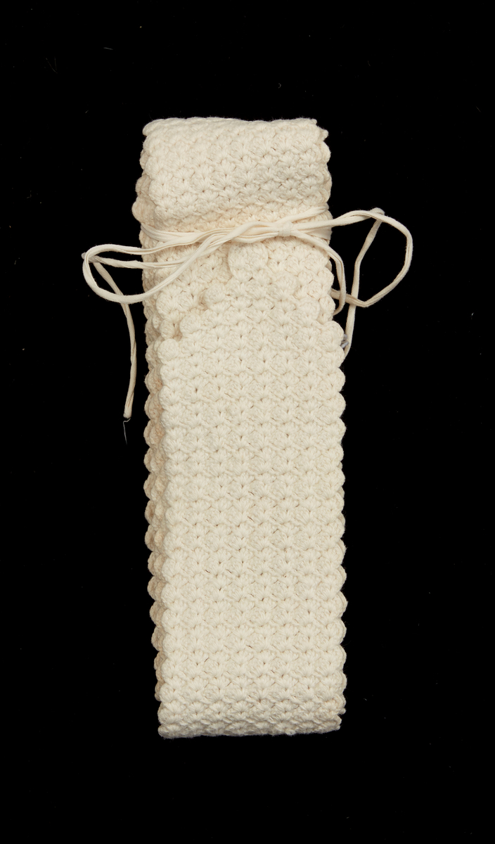 Barnlinda i virkade stolpmaskor i grupper av vit bomullsgarn. En kortsida avslutad i spets med ett påsytt vitt maskinvävt bomullsband för knytning.