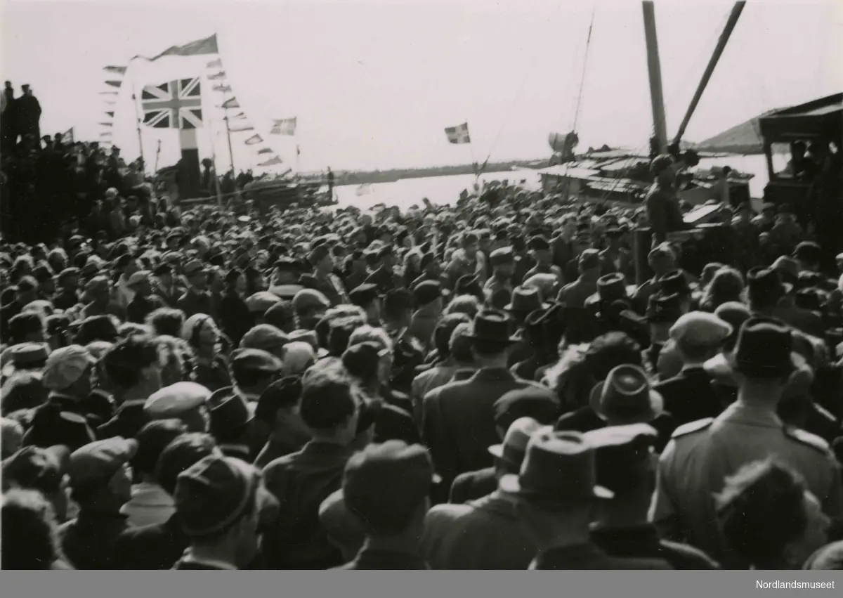 Uklart bilde av en folkemengde. Skip i bakgrunnen. Bilde tatt i Bodø under feiring av freden etter okkupasjonen 1945.