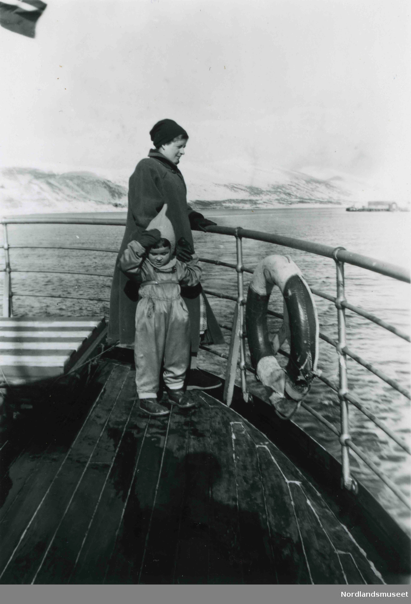 En kvinne og et lite barn ombord i en båt. I bakgrunnen sees snødekte fjell.