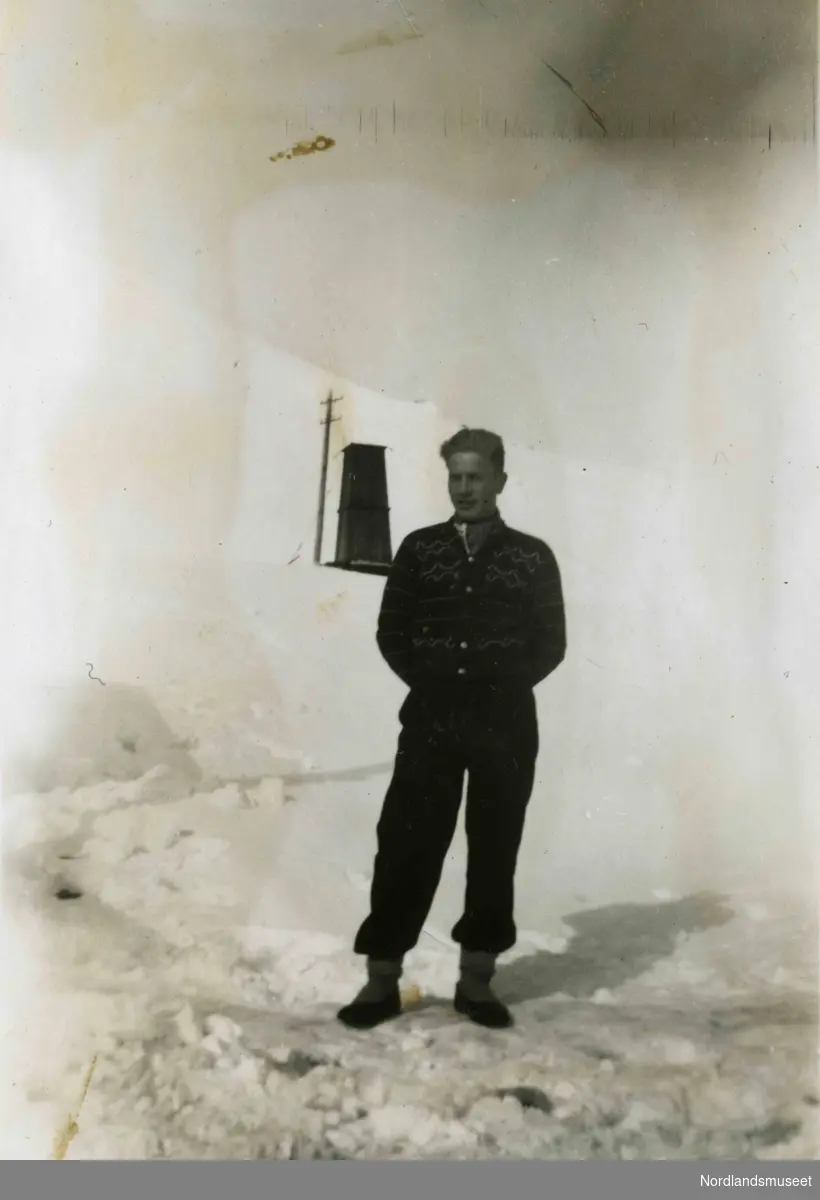 En ung mann i strikkejakke står utendørs i snøen. Bildetekst: "Sagmo, Sulitjelma".