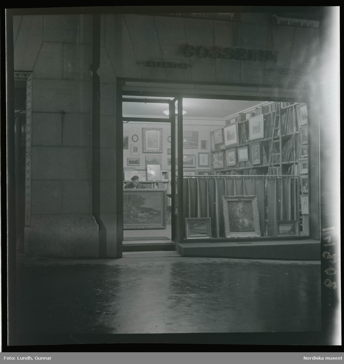 1950. Paris. En man sittter inne i en butik med konst, kväll