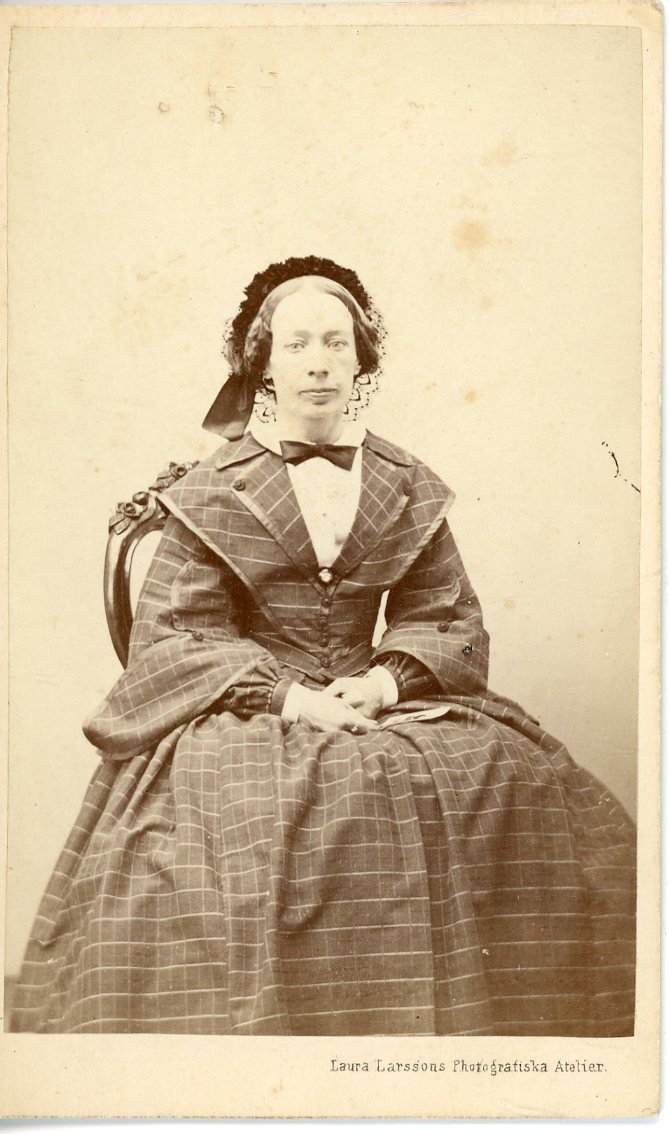 Porträtt av en okänd kvinna i rutig klänning som sitter på en stol.