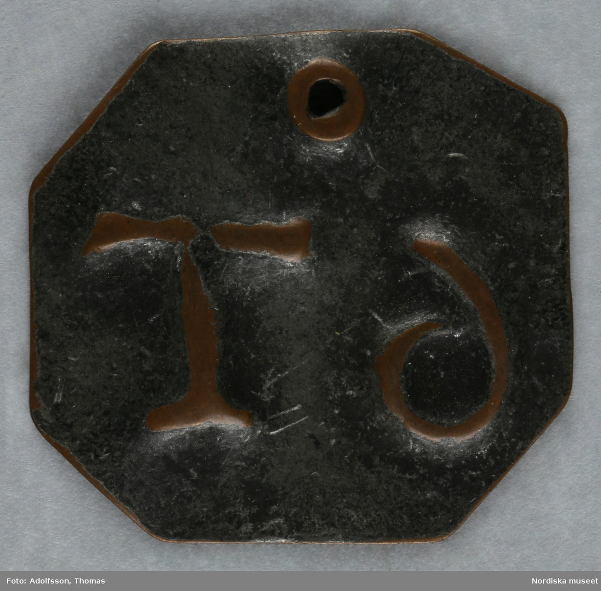 Pollett, av koppar, fyrkantig med avklippta hörn, ett hål, präglad text: "6 T".