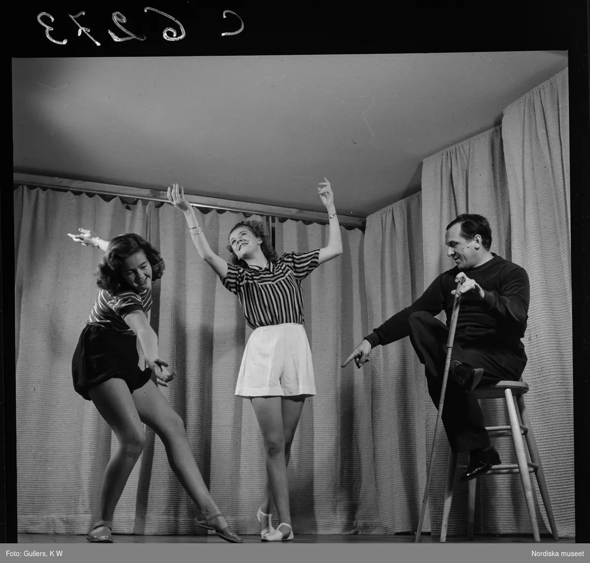 505 Wityansky Teaterskola för Allers. Två kvinnliga teaterelever  dansar, en man sitter på en pall med en käpp i handen och instruerar.