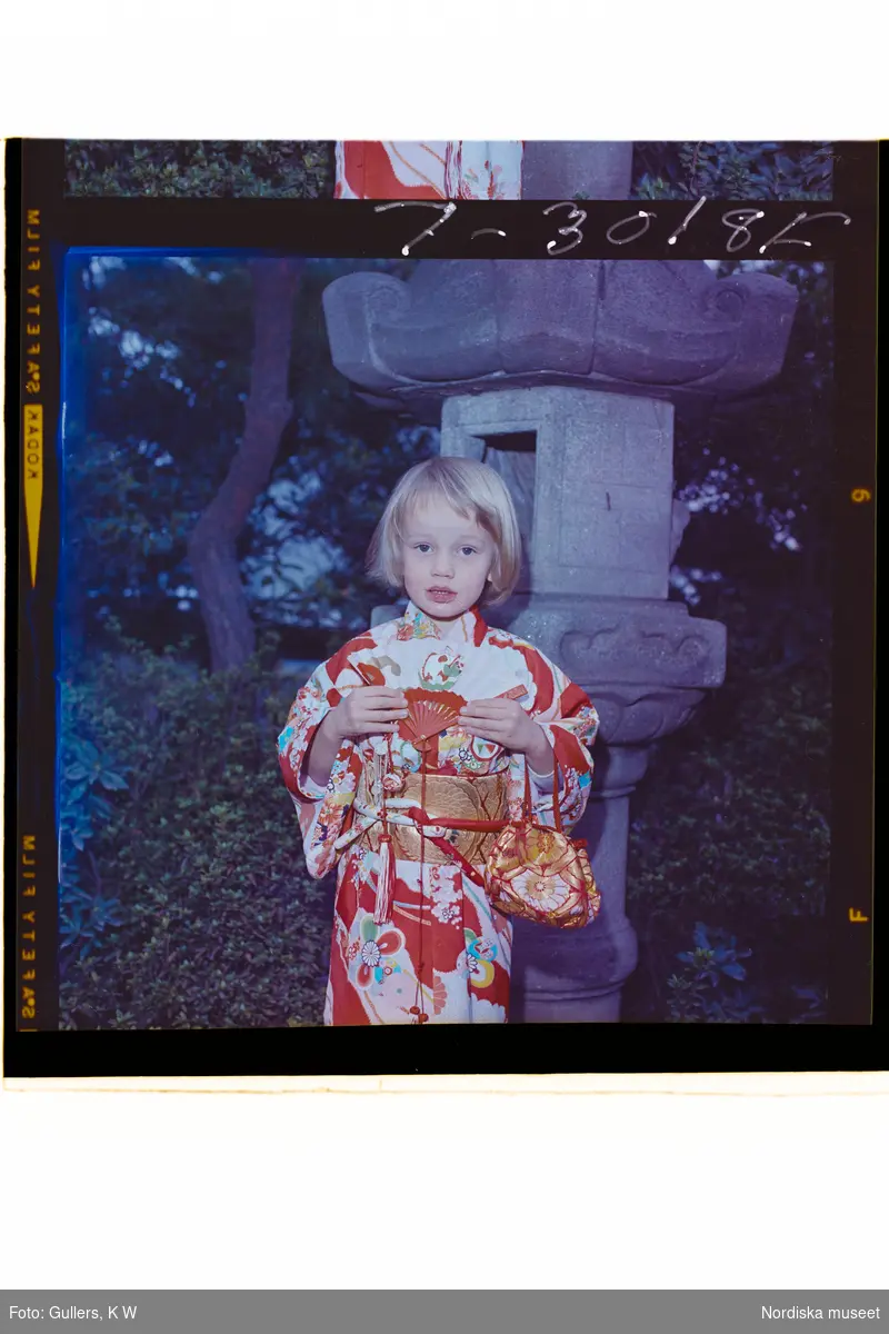 585/8 Facit Tokyo Daberg. Porträtt av ett barn i kimono som står i en trädgård.