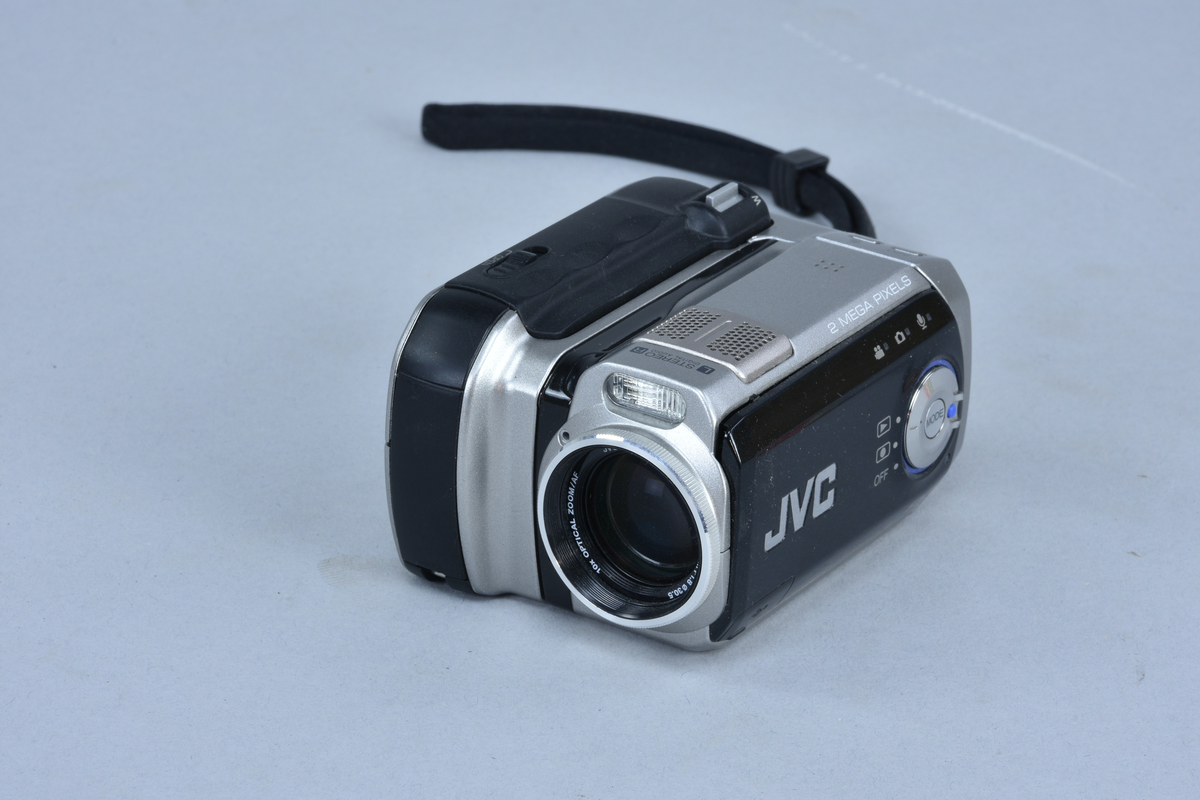Digital mediakamera 2 megapixlar med inbyggd stereomikrofon JVC typ GZ-MC200E nr 00000001 (förserieexemplar). För lagring på minneskort typ Microdrive. Zoom 1:1.8 brännvidd 4.5-45 mm med autofokus, 10x "optical zoom". Vridbar så att displayen på baksidan är lätt att se. Plats för Microdrive med Compact Flash II -anslutning samt batteri.