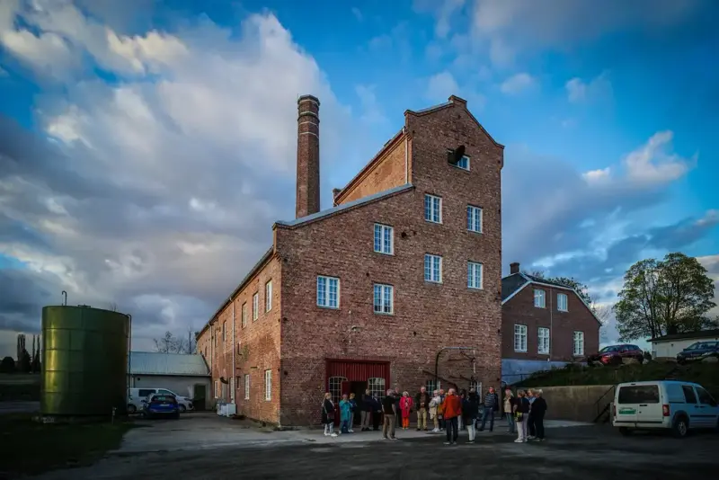 fotografi av Atlungstad Brenneri sett nedenfra. Bildet viser folk på vei inn for en omvisning i brenneriet