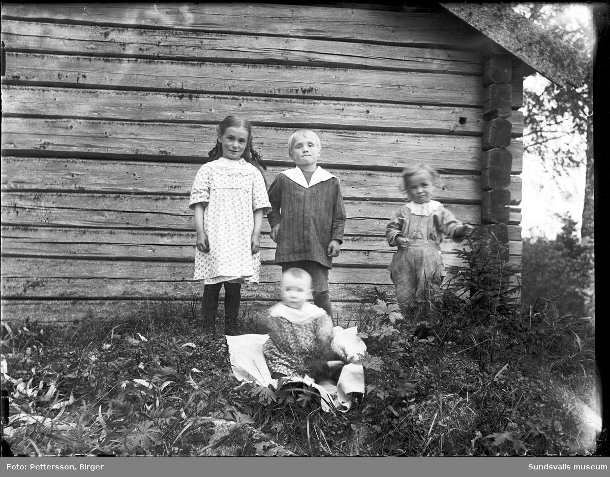 Två familjeporträtt med mor, far och fyra barn invid en liten timrad stuga. På den andra bilden är det enbart syskonskaran.