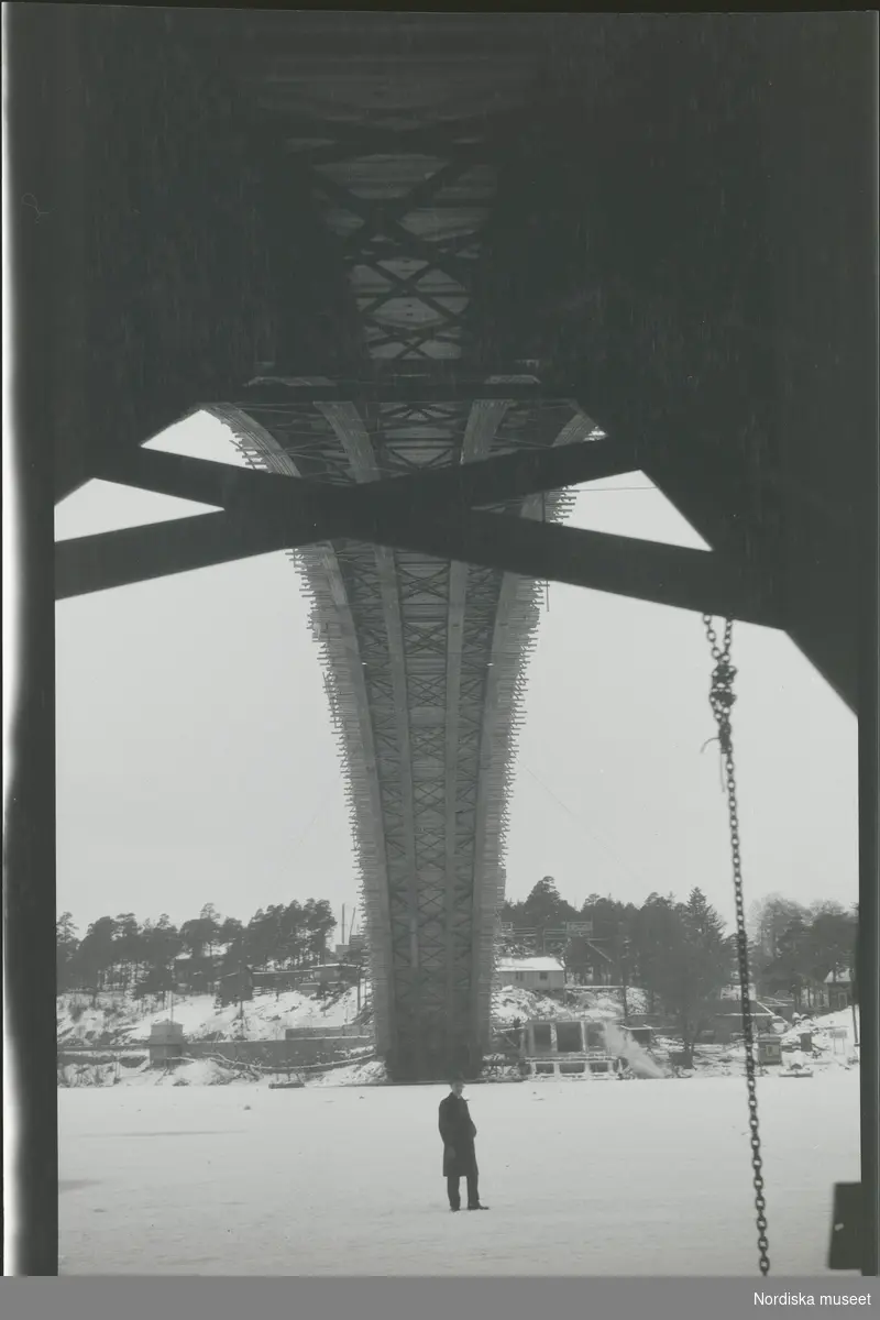 En man står på isen under en bro som håller på att byggas.