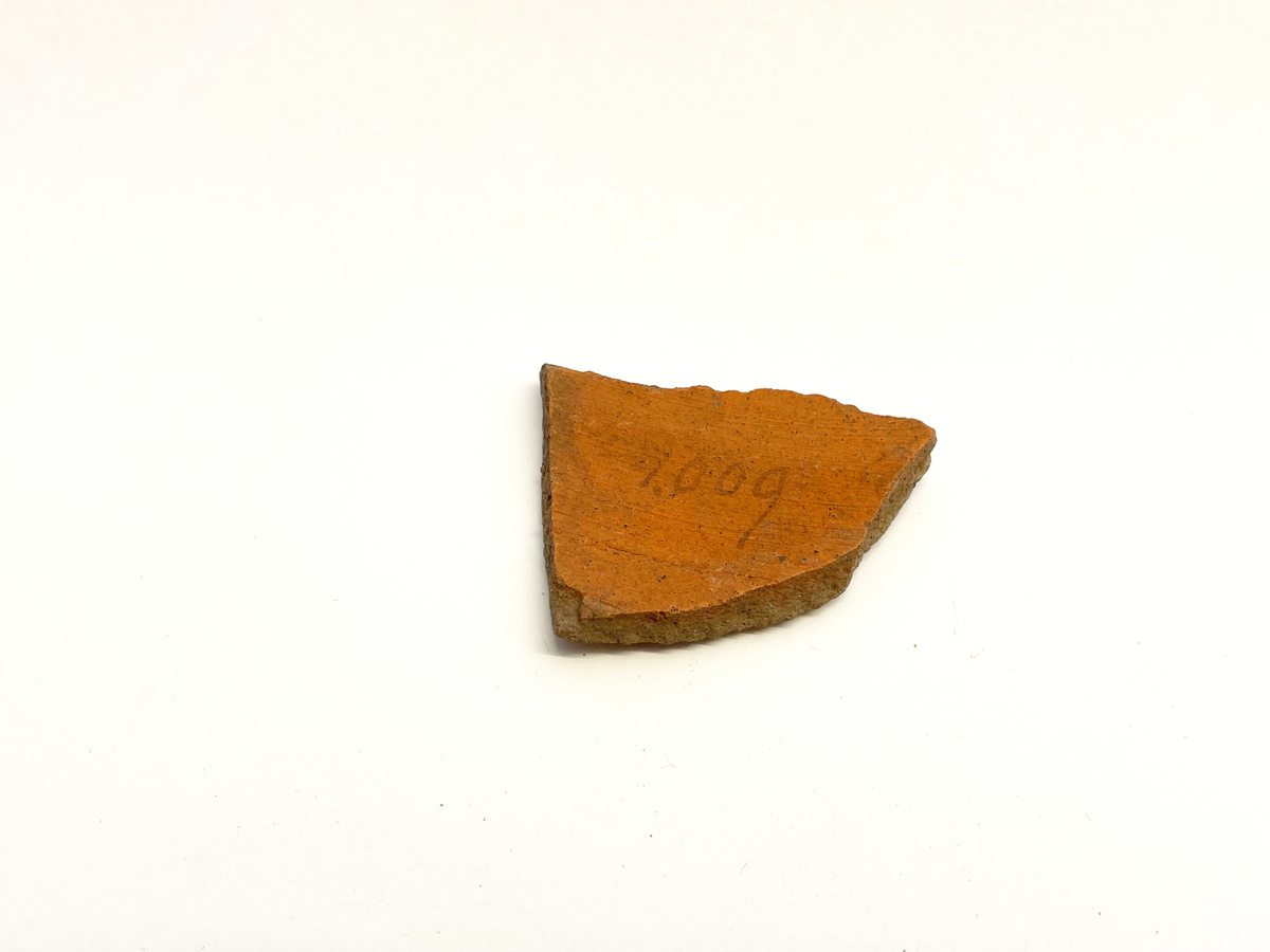 Ett bukfragment av äldre (?) rödgods med senapsgul glasyr på utsidan. Drejlinjer. Möjligen del av en kanna eller gryta. Mycket lik M 48845-38a samt 41 och 42.